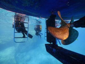 Propeller of the boat underwater scuba divers climbing up the ladder.