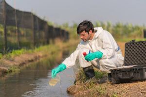 A technician in full body protective suit collecting sample of contaminated water.